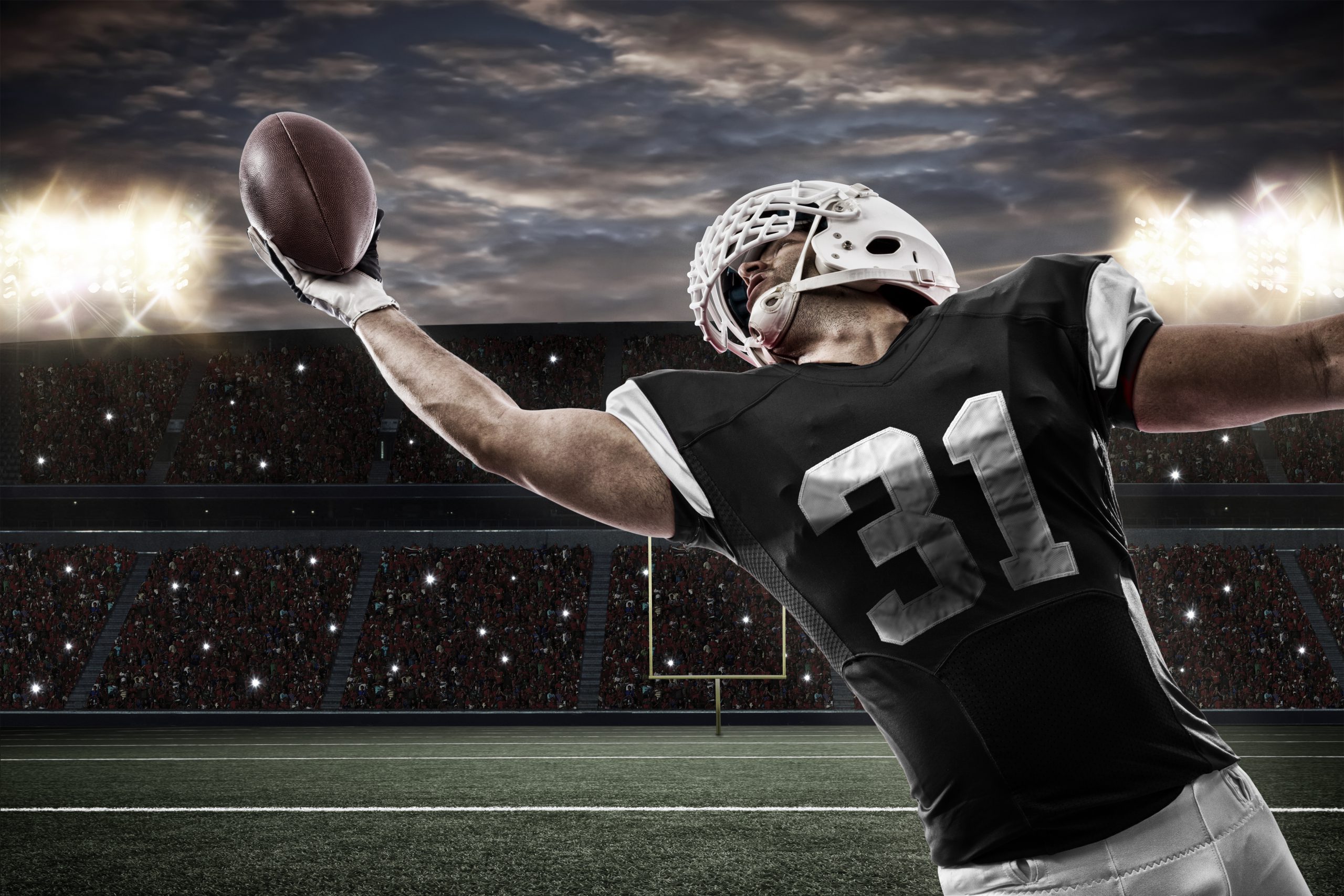 Football Player with a Black uniform catching a ball on a stadium.
